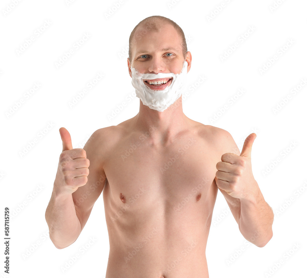 Young man with shaving foam on face showing thumb-up against white background