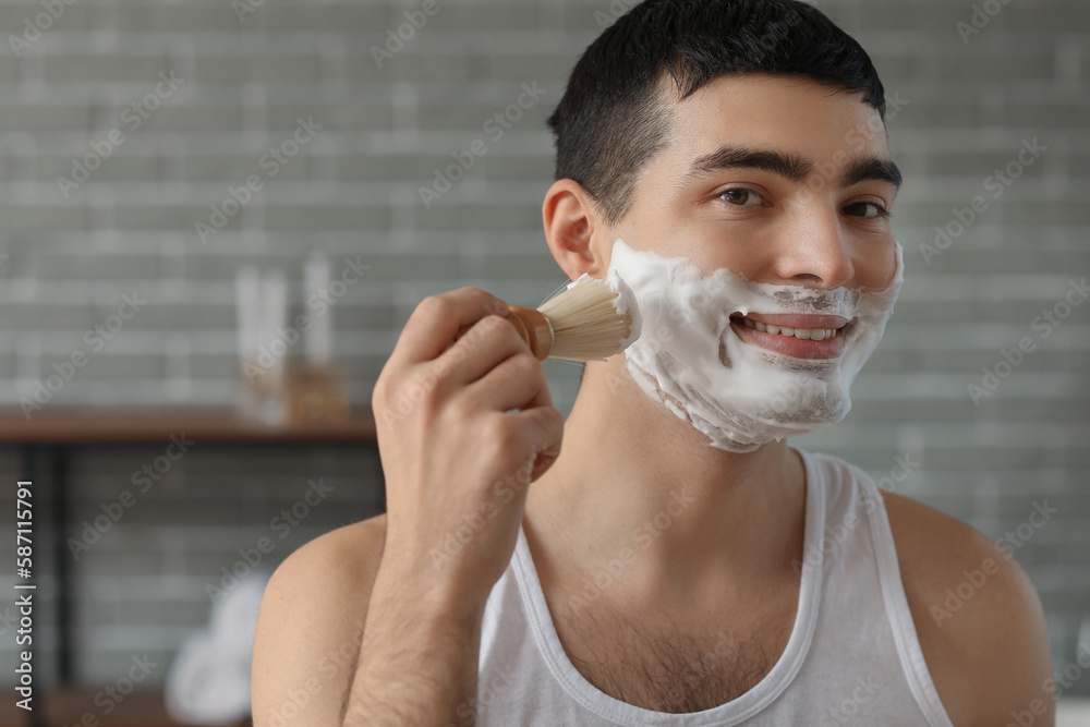 Young man applying shaving foam onto face in bathroom