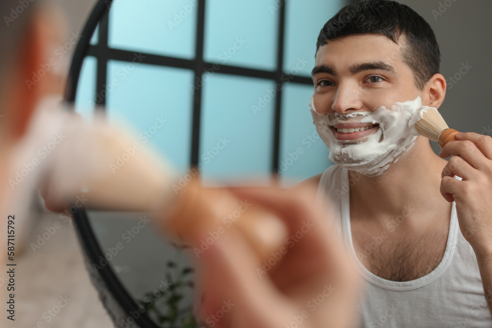 Young man applying shaving foam onto face in bathroom