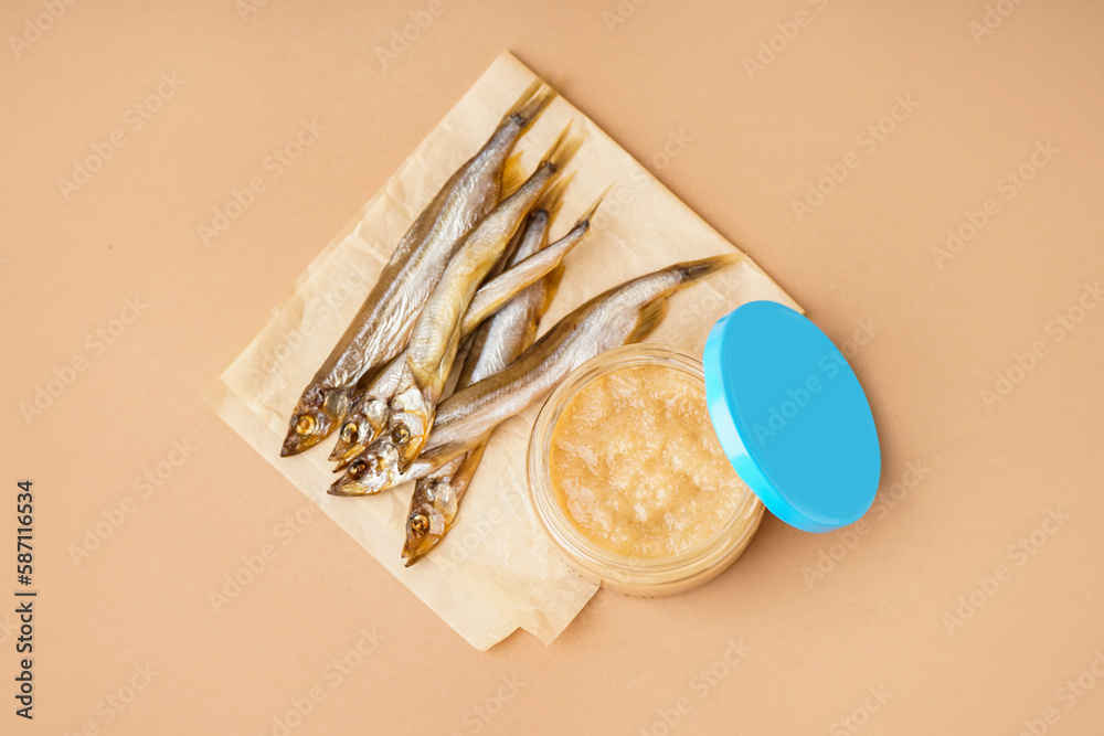 Jar of caviar and parchment with smoked capelin fish on brown background