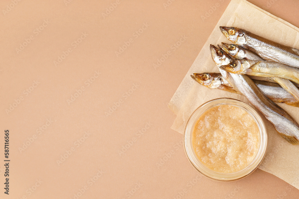 Jar of caviar and parchment with smoked capelin fish on brown background