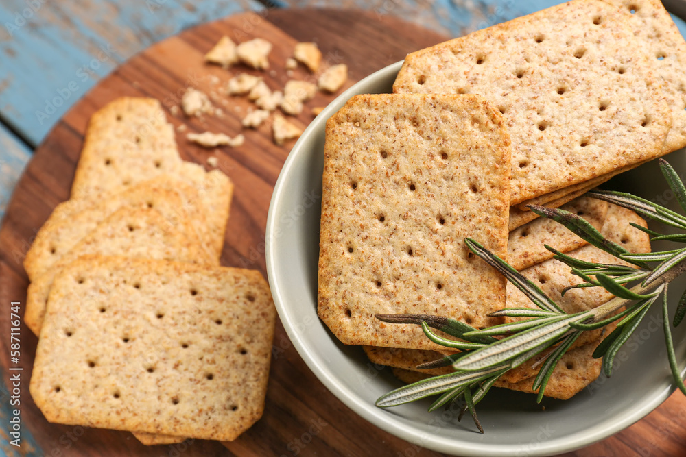 Bowl with tasty crackers and rosemary on wooden board, closeup