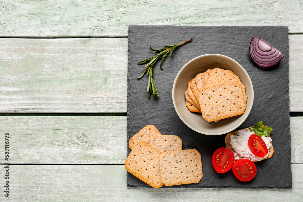 Slate board with tasty crackers, cream cheese and tomatoes on green wooden background