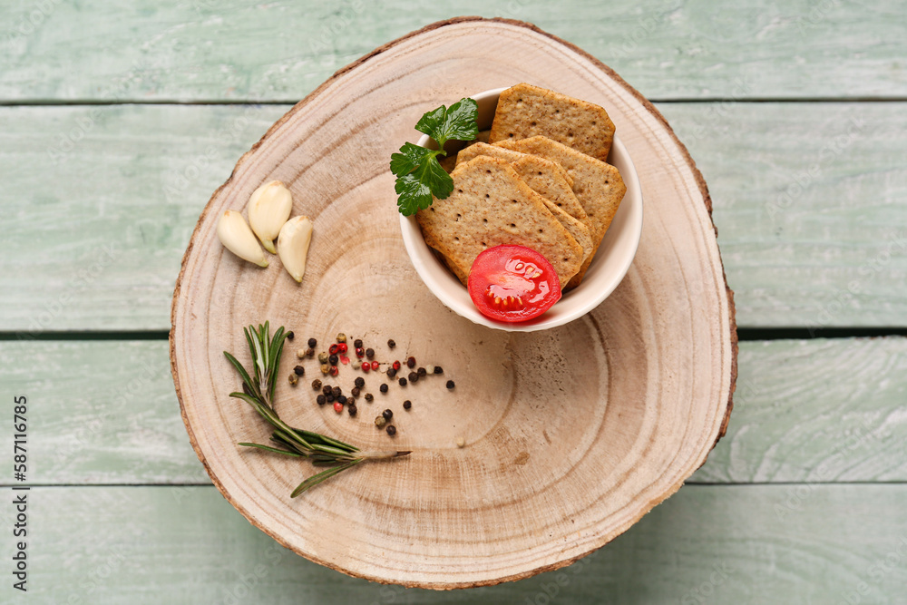 Stand with bowl of tasty crackers, garlic, peppercorn and tomato on green wooden background