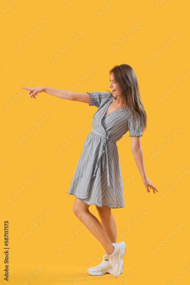 Beautiful woman in striped dress pointing at something on yellow background