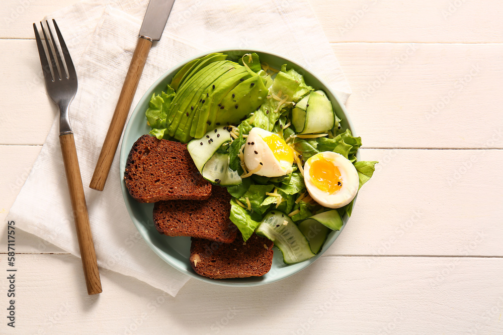 Plate of delicious salad with boiled eggs and avocado on white wooden background