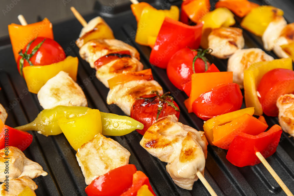 Modern electric grill with tasty chicken skewers and vegetables on table, closeup