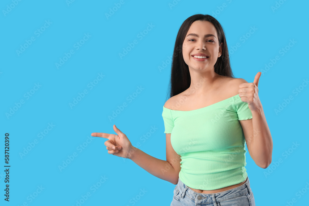 Beautiful young woman pointing at something on blue background