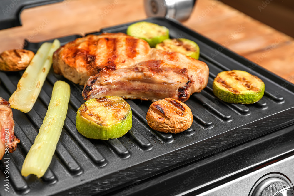 Modern electric grill with tasty steak and vegetables on table, closeup