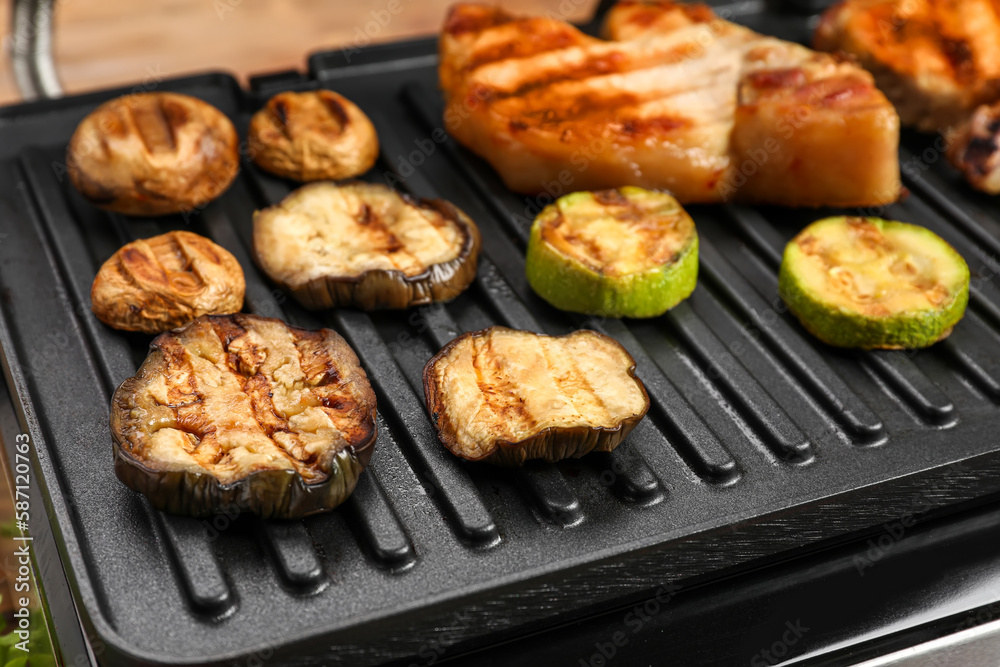 Modern electric grill with tasty vegetables and steaks on table, closeup