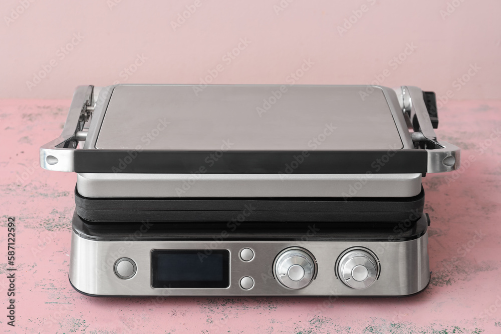 Modern electric grill with closed lid on pink table