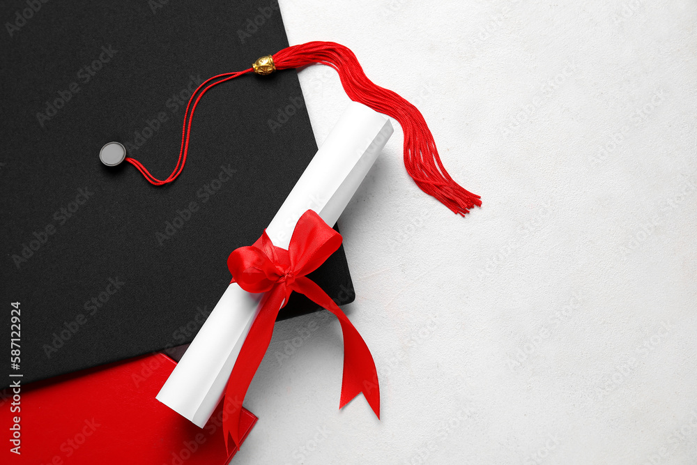 Diploma with red ribbon and graduation hat on white table