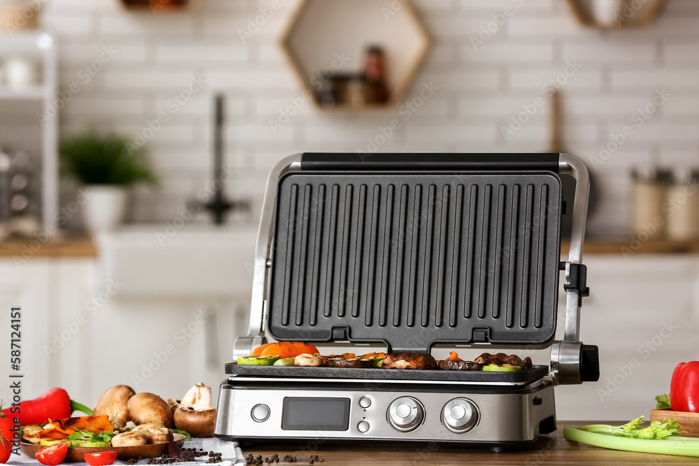 Modern electric grill with tasty vegetables on table in kitchen