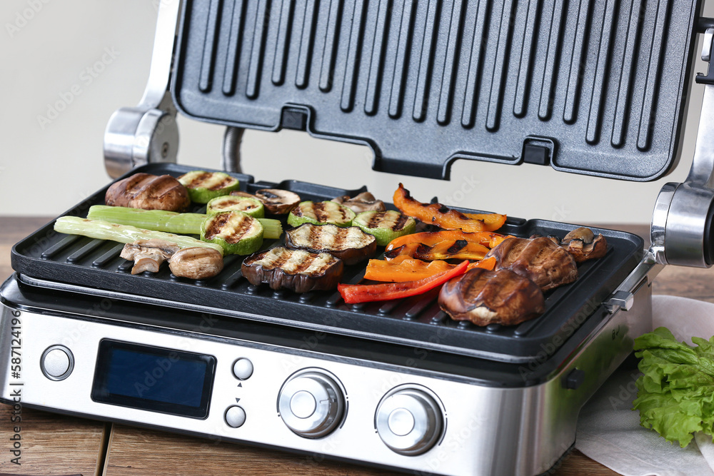 Modern electric grill with tasty vegetables on table in kitchen