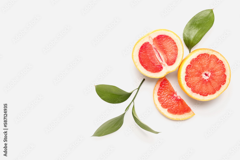 Composition with cut juicy grapefruit and plant leaves on white background