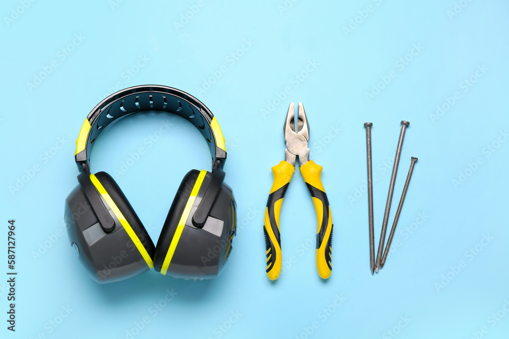 Hearing protectors, pliers and nails on blue background