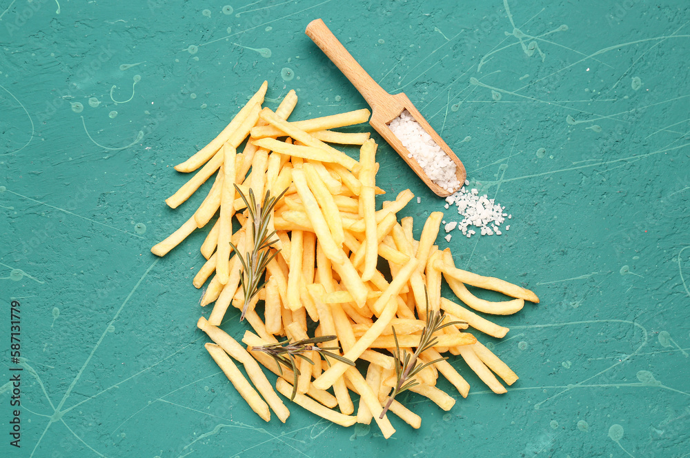 Tasty french fries and salt on green background