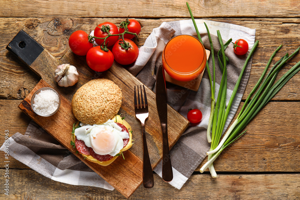 Board with tasty egg Benedict, tomatoes and glass of juice on wooden background