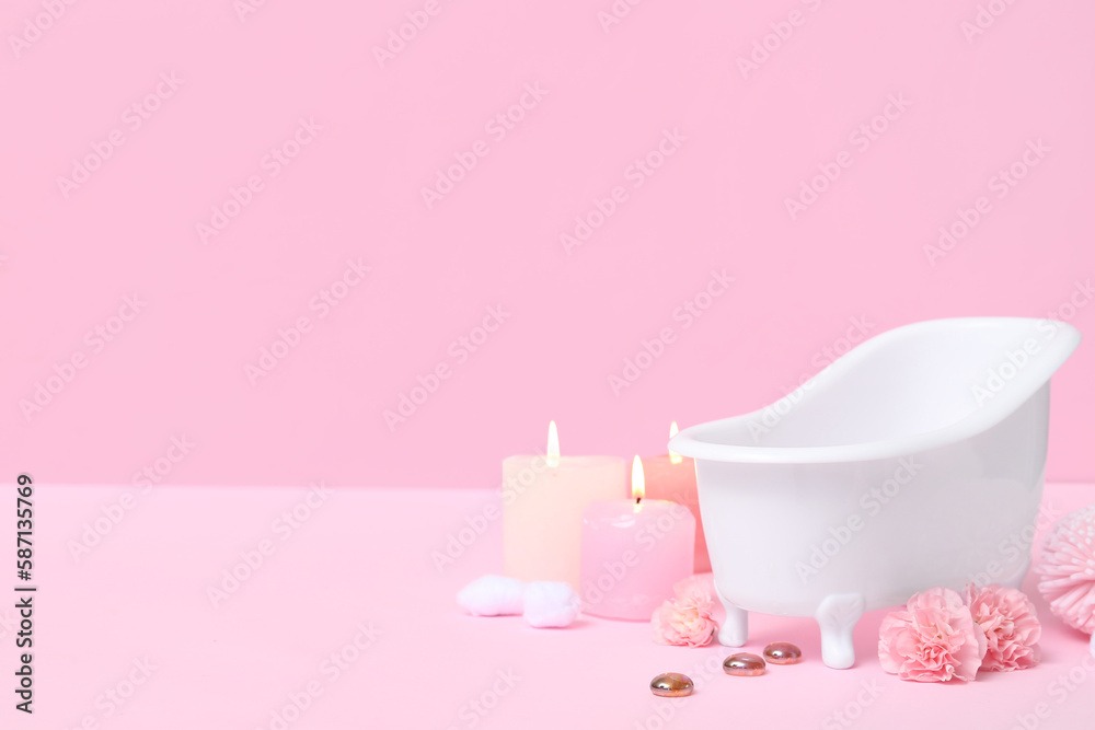 Small bathtub, burning candles and carnation flowers on color background