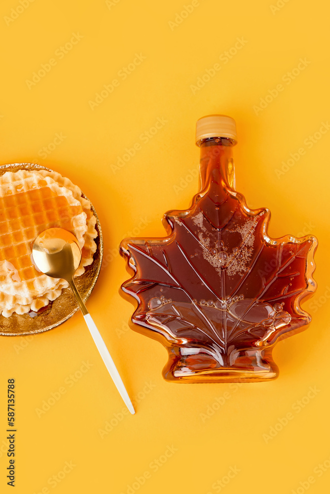 Waffles with bottle and spoon of tasty maple syrup on yellow background