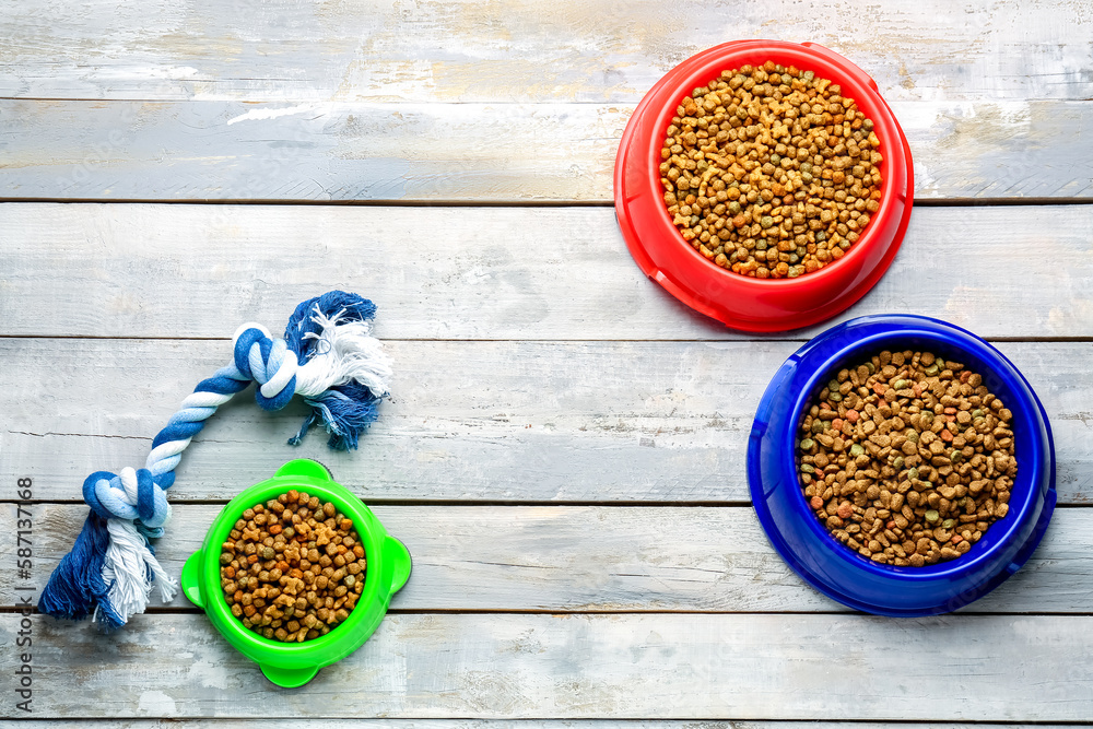 Bowls of dry pet food with toy on light wooden background