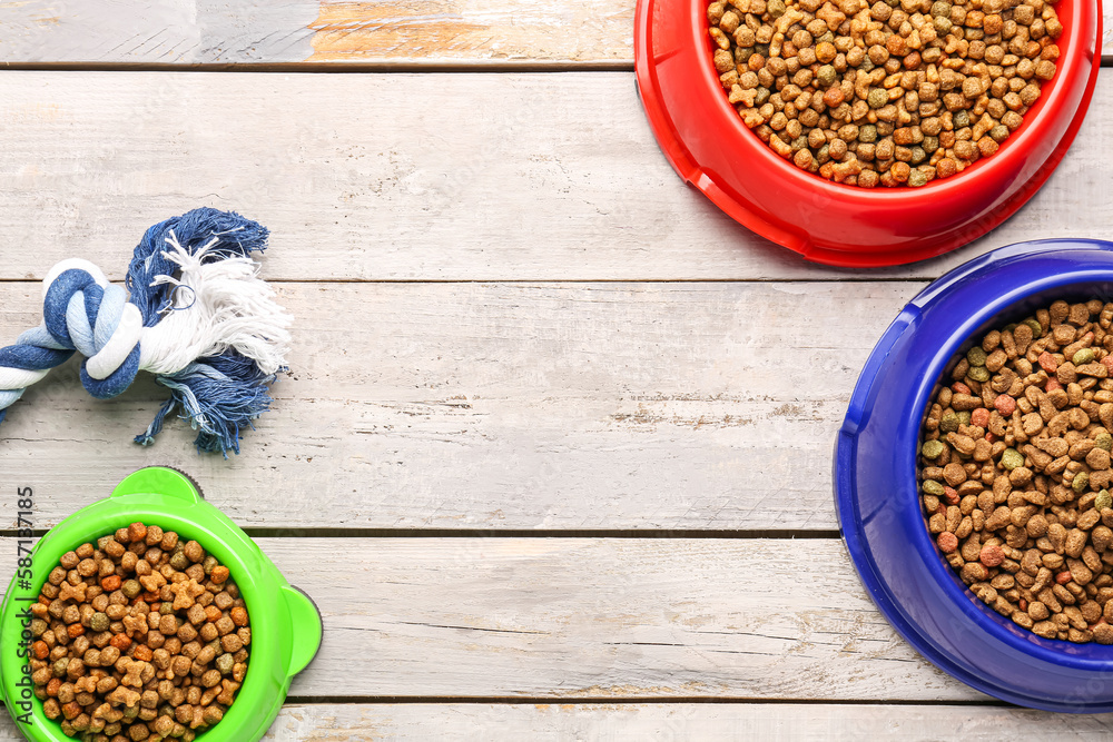 Bowls of dry pet food with toy on light wooden background