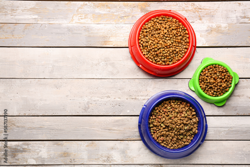 Bowls of dry pet food on light wooden background