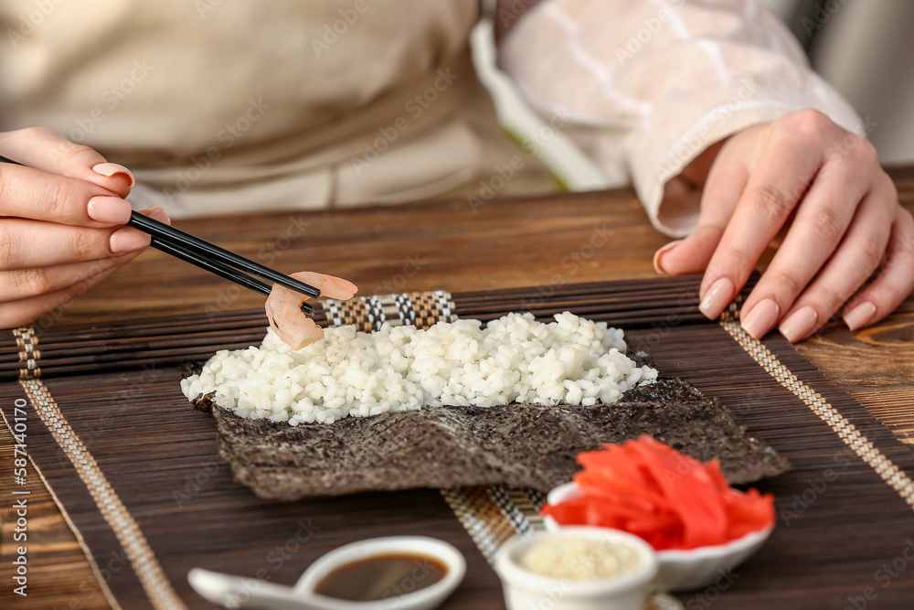 Woman preparing sushi rolls at table, closeup