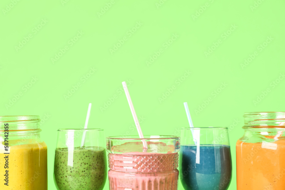 Glasses of colorful smoothie on green background