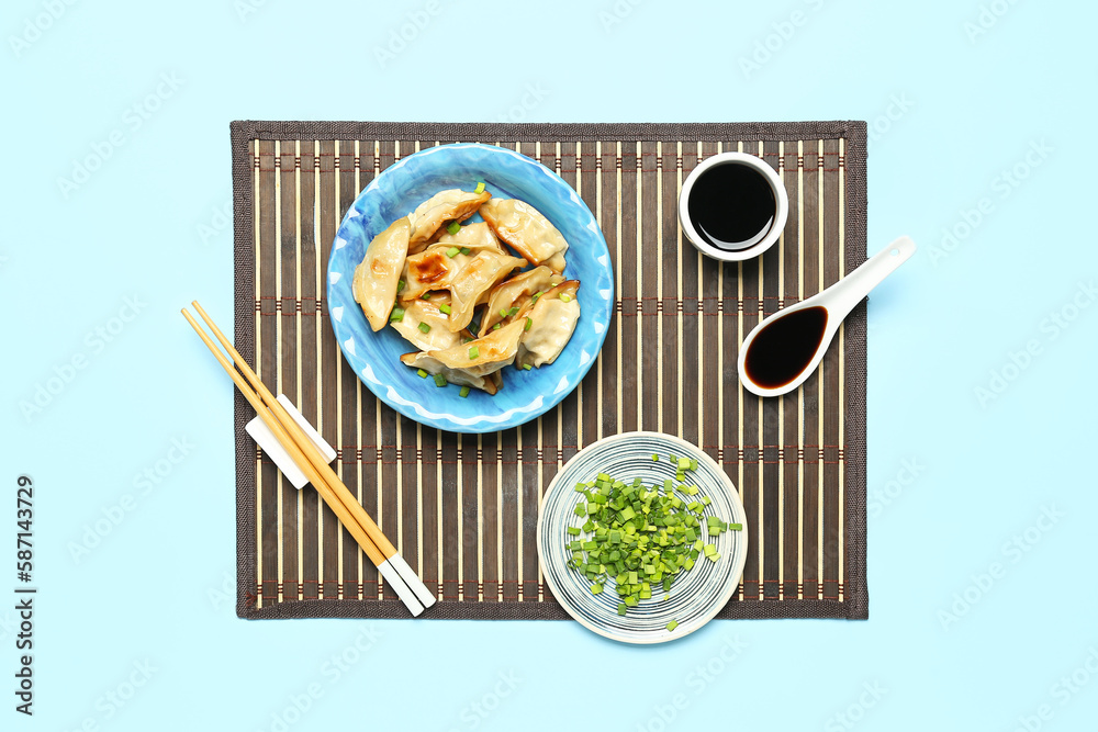 Plate with tasty Chinese jiaozi, onion and sauce on blue background