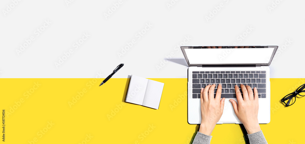 Person using a laptop computer with a notebook and eyeglasses - Flat lay