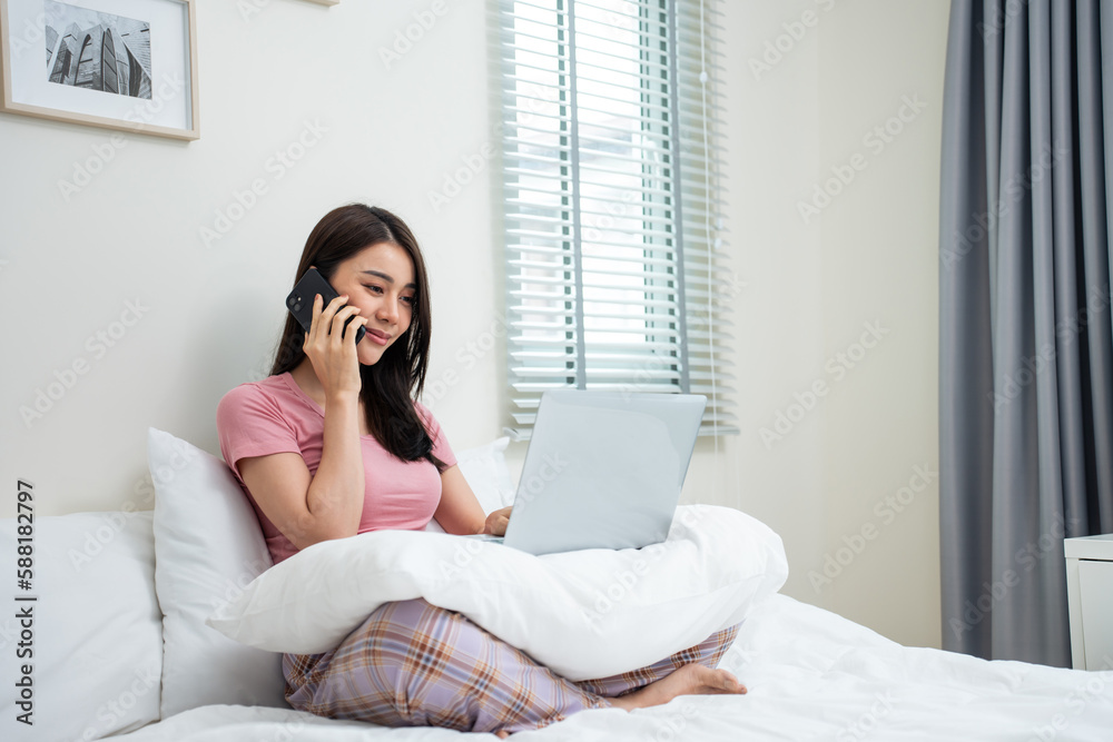 Asian businesswoman talk on phone and typing laptop keyboard in house. 