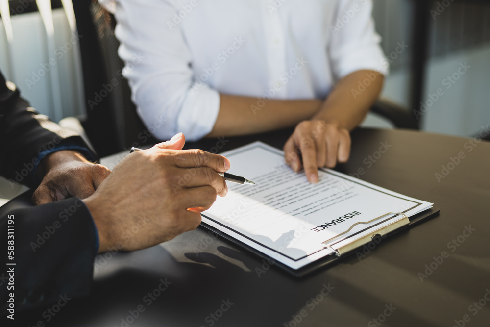 Businessman in suit in his office showing an insurance policy and pointing with a pen where the poli