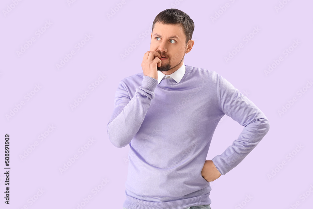 Handsome man biting nails on lilac background