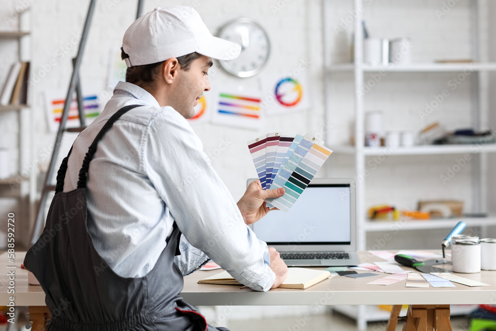 Male painter with color palettes writing in notebook at table