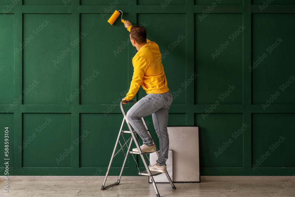 Young man with roller and ladder painting green wall