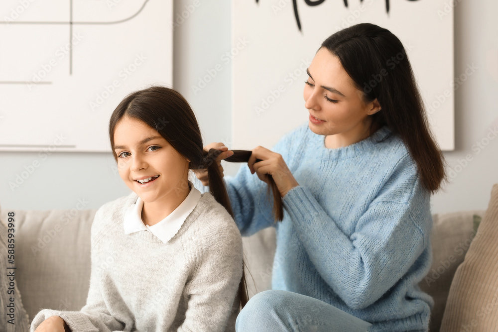 Mother doing hair of her little daughter at home