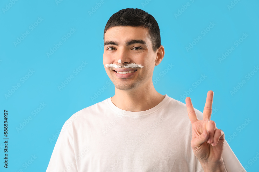 Young man with shaving foam on face against light blue background