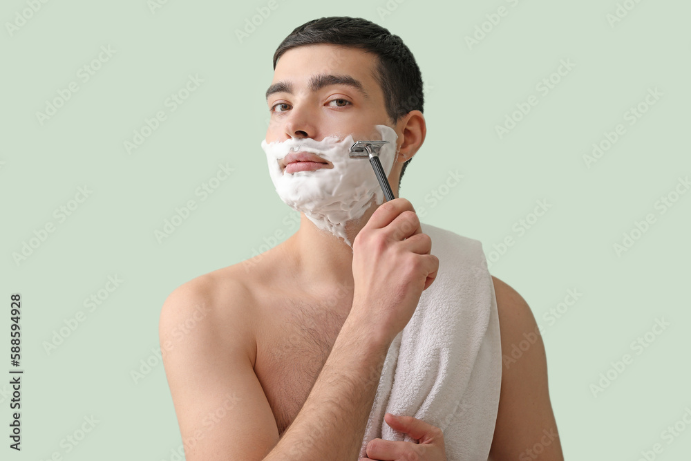 Young man shaving against green background