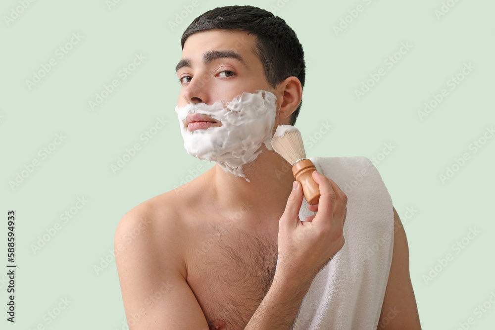 Young man shaving against green background