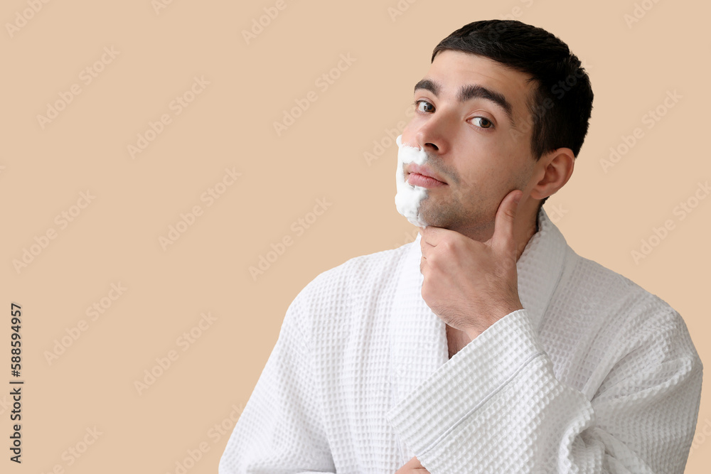 Young man with shaving foam on face against beige background