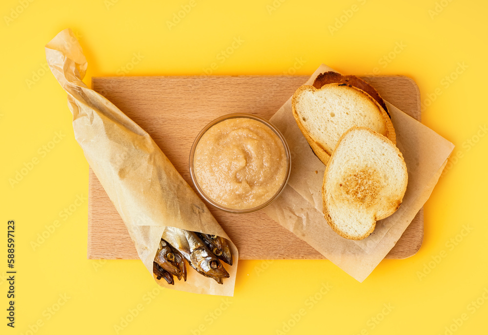 Bowl with caviar, smoked capelin wrapped in parchment and fried baguette on yellow background