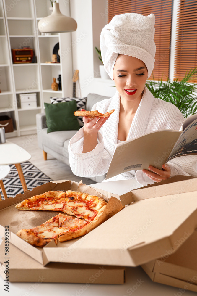 Young woman in bathrobe with tasty pizza reading magazine at home