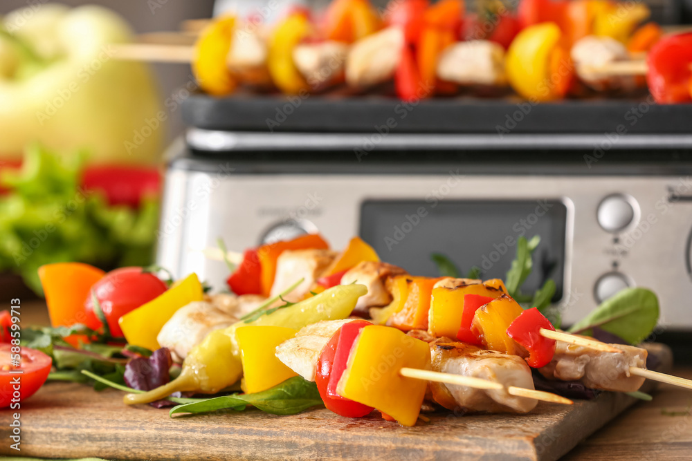 Wooden board with grilled chicken skewers and vegetables on table in kitchen