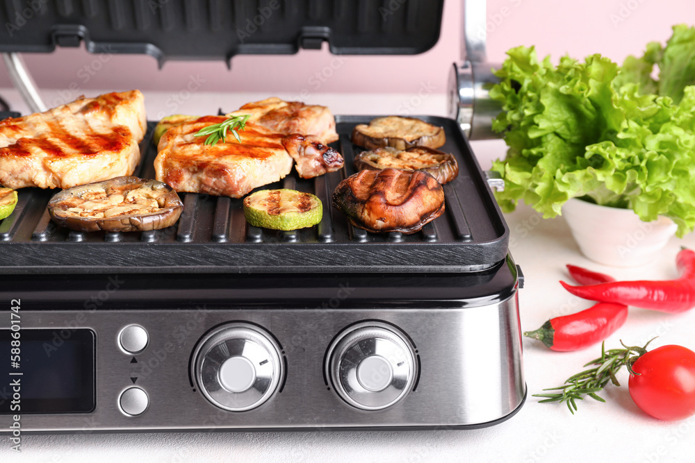 Modern electric grill with tasty steaks and vegetables on light background, closeup