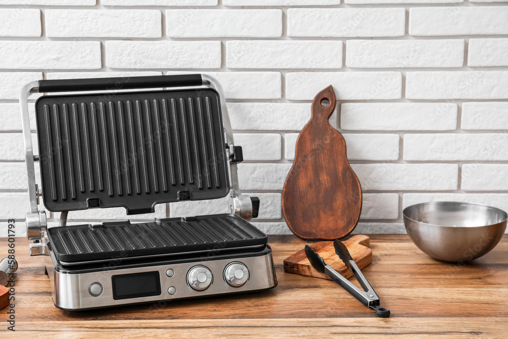 Modern electric grill on table near white brick wall