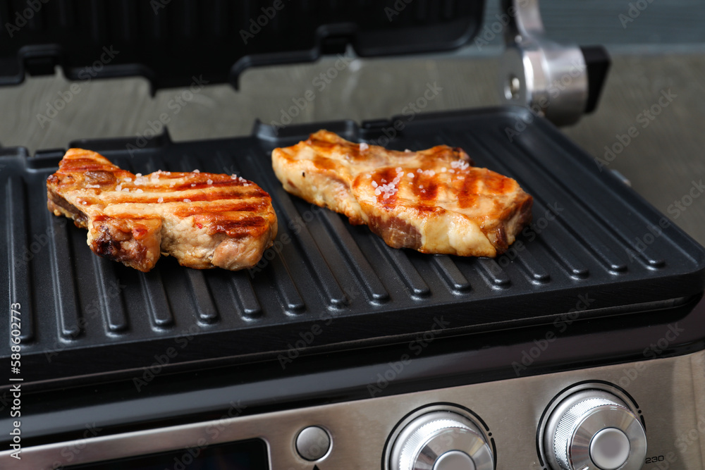 Modern electric grill with delicious steaks on grey wooden table