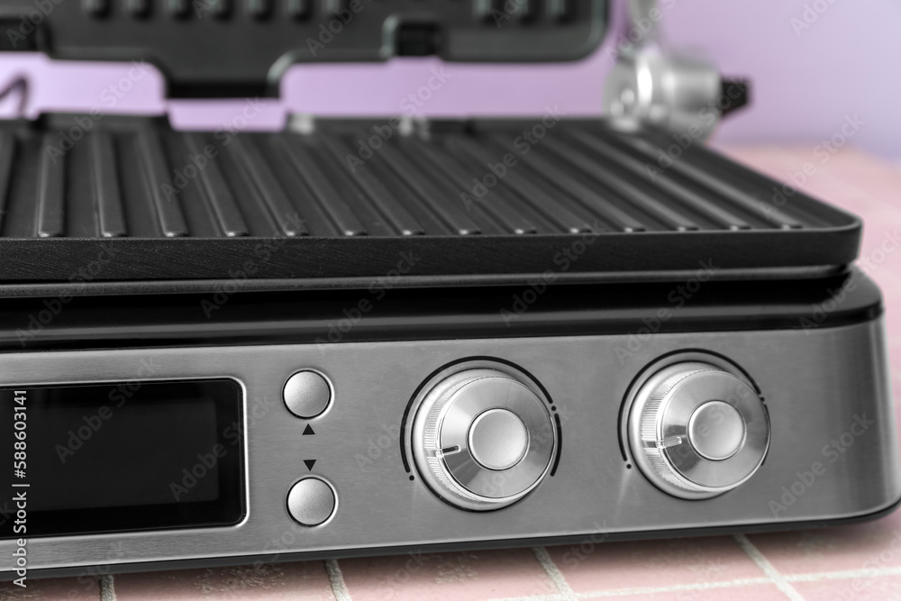 Control panel of modern electric grill on pink tile table, closeup