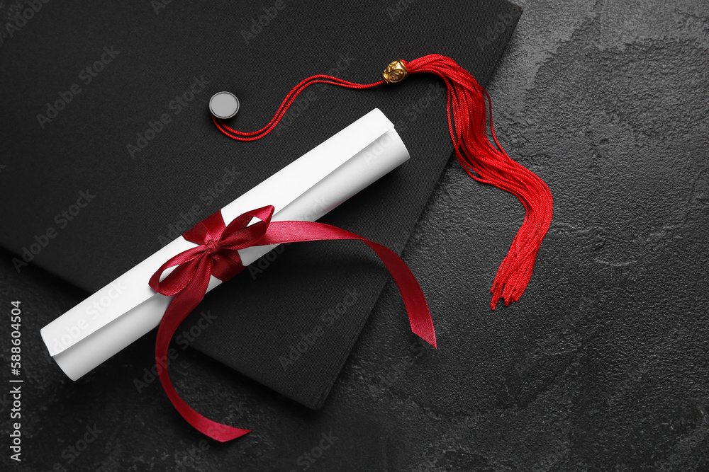 Diploma with red ribbon and graduation hat on black table