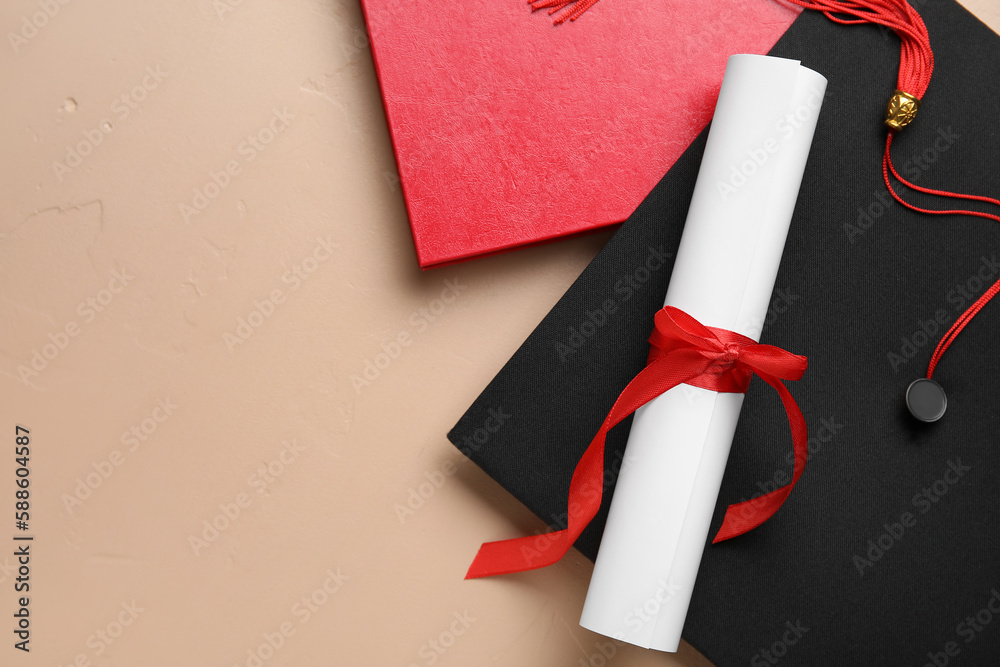 Diploma with red ribbon, graduation hat and book on beige background